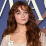 Joey King poses on the red carpet at the “Practical Magic 2” premiere with curly, wispy “Wicked Bangs” and long auburn waves.